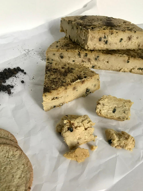 An unwrapped wedge of plant-based cashew e pepe che*se with slices cut from the wedge