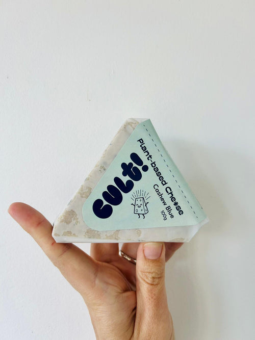 A hand holding a wedge of Cashew Blue from Cult! Plat-based Che*se